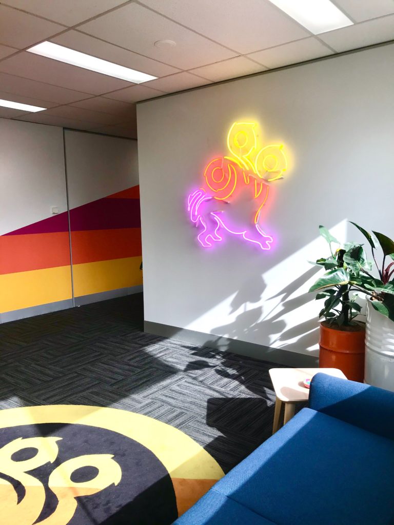 An office wall featuring a neon sign version of the League of Geeks logo